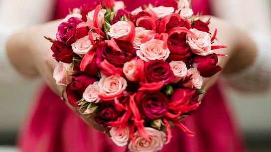 © Österreichisches Blumenbüro Eine Frau hält einen runden Blumenstrauß aus roten und rosa Rosen in die Kamera.