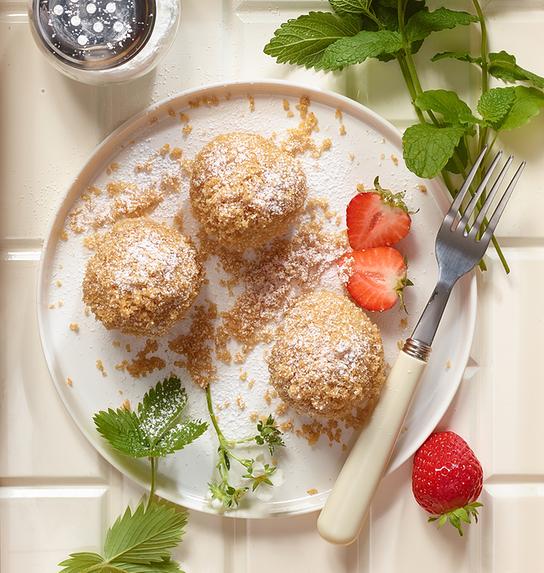 © Stephanie Golser Auf einem Tablett liegen kleine süße Knödel mit Bröseln, Erdbeeren auf einem Teller und frischen Kräutern angerichtet.