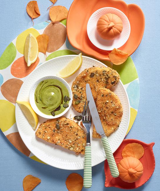 Gebackener Kürbis in Panko-Kürbiskern-Panade mit Kürbiskernöl-Mayonnaise ist farbenfroh auf einem gedeckten Tisch angerichtet.