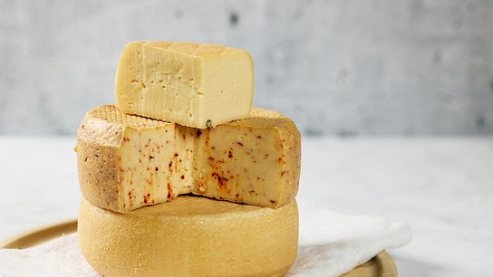 Mehrere Laibe und Stücke von hellem Käse sind auf einem Holzbrett gestapelt.