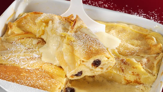 © Stockfood/Karl Newedel Überbackene Topfenpalatschinken mit goldbrauner Oberfläche werden mit Vanillesauce serviert und mit Staubzucker bestreut.