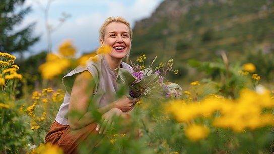 © iStock/miniseries Eine Frau kniet in einer blühenden Wiese und hält einen bunten Strauß Wildblumen.