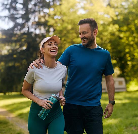 © iStock/Drazen Zigic Ein sportlich gekleidetes Paar geht eng nebeneinander auf einem Waldweg spazieren.