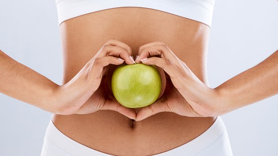 Eine Frau hält einen grünen Apfel mit beiden Händen vor dem Bauch als Symbol für Darmgesundheit.