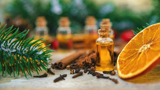 © 123RF/Yanadjana Kleine Flasche mit gelb-goldenem Öl, umgeben von Zimtstangen, Nelken, Orangenscheibe und Tannenzweigen.