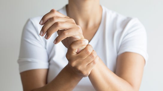 © iStock/Solidcolours Eine Frau greift sich mit einer Hand an das gegenüberliegende Handgelenk vor neutralem Hintergrund.