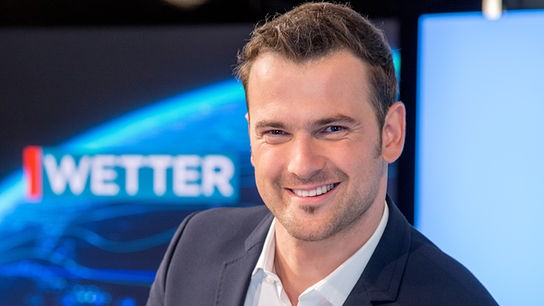 Sigi Fink steht an einem Pult vor einem Bildschirm mit Wettergrafik.