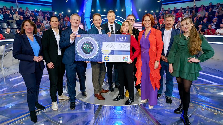 © ORF/Guido Engels Gruppenfoto mit Claudia Schmidberger-Slond, Natalie Flatz, Daniel Bohmann, Jürgen Blematl, Armin Assinger, Lisa Zuckerstätter, Max Stiegl, Maya Hakvoort, Hans Bürger und Anna Strigl, die einen großen "120.000 Euro"-Scheck für LICHT INS DUNKEL in ihren Händen halten im Studio.