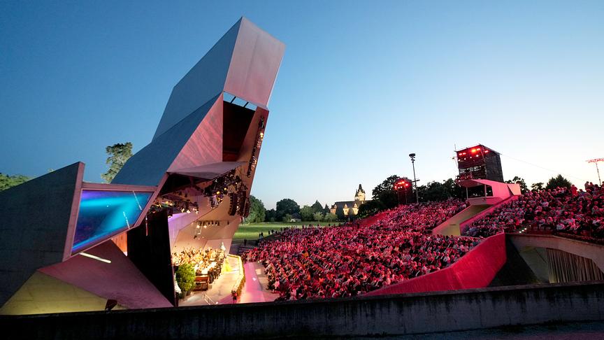 Der Wolkenturm Grafenegg, eine moderne Freiluftbühne mit markanter Architektur, ist bei Abendlicht voll besetzt, während die Sommernachtsgala vor großem Publikum unter freiem Himmel stattfindet.