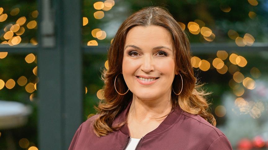 Porträt von Barbara Karlich vor abednlich-beleuchtetem verschwommenen Hintergrund