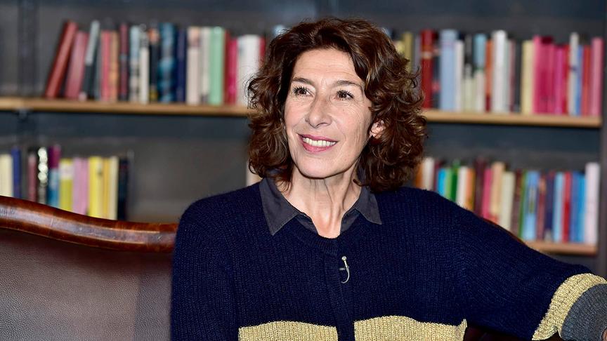 Adele Neuhauser lächelnd vor einem Bücherregal