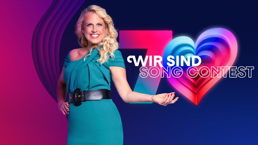 Barbara Schöneberger steht vor einem farbenfrohen, modern gestalteten Logo mit der Zahl 7 und einem leuchtenden Herzsymbol symbolisch für die Zahl 0 und dem Schriftzug „WIR SIND SONG CONTEST“