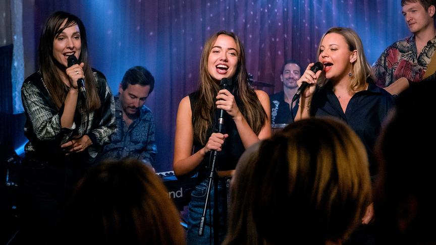 © ORF/E&A Film/Anjeza Cikopano Agnes Hausmann, Mara Romei und Katharina Straßer stehen auf einer Bühne und singen vor einem Publikum, begleitet von einer Band im Hintergrund.