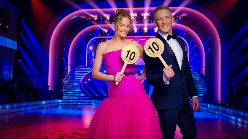 Mirjam Weichselbraun im Ballkleid und Andi Knoll im Smoking halten auf der bunt beleuchteten "Dancing Stars"-Bühne jeweils eine Wertungstafel mit der Zahl zehn.
