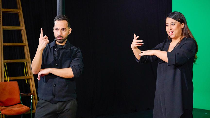 Alice Hu Xiaoshu mit Coach Delil Yilmaz stehen in einem Studio und führen mit ihren Händen Gesten aus.