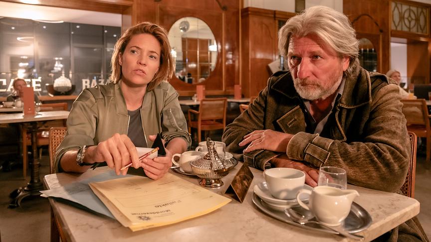 © ORF/Satel Film/Lisa Kutzelnig Lu Frey und Hubert Mur sitzen in einem Café und beobachten etwas.