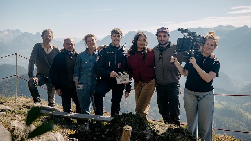  Florian Gebhardt (Produzent), Arash T. Riahi (Regie), Caroline Frank (Dr. Wilder), Anton Widauer (Jona Egger), Salka Weber (Alex Fink), Arman T. Riahi (Regie), Anna Hawliczek (DoP) posieren mit Filmklappe und Kamera vor einer Alpenkulisse.