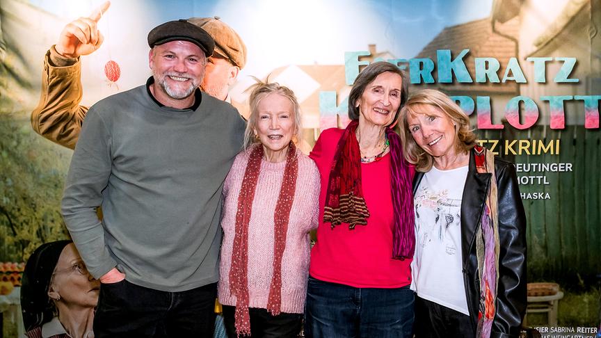 Gruppenfoto mit Thomas Stipsits, Erika Mottl, Linde Prelog und Erika Deutinger vor dem Plakat zum „Eierkratz-Komplott“