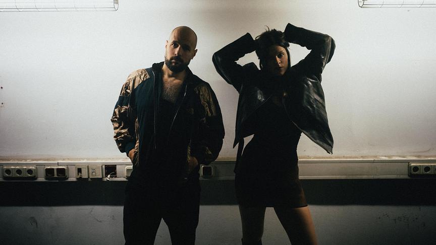 Das Duo von HVOB posiert in einem industriell wirkenden Raum unter Neonleuchten.