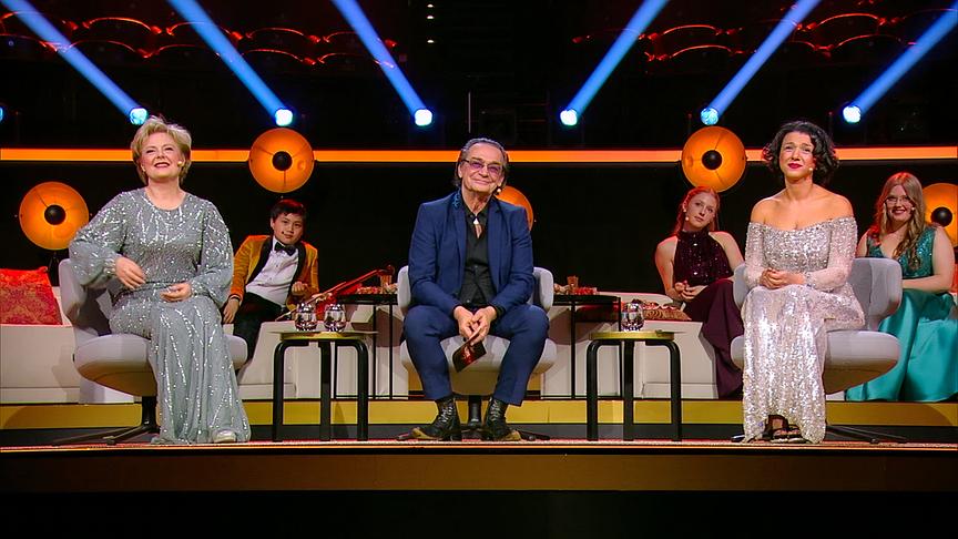 Die Starjury mit Khatia Buniatishvili, Ildikó Raimondi und Christian Kolonovits sitzen nebeneinander auf der festlich beleuchteten TV‑Bühne.
