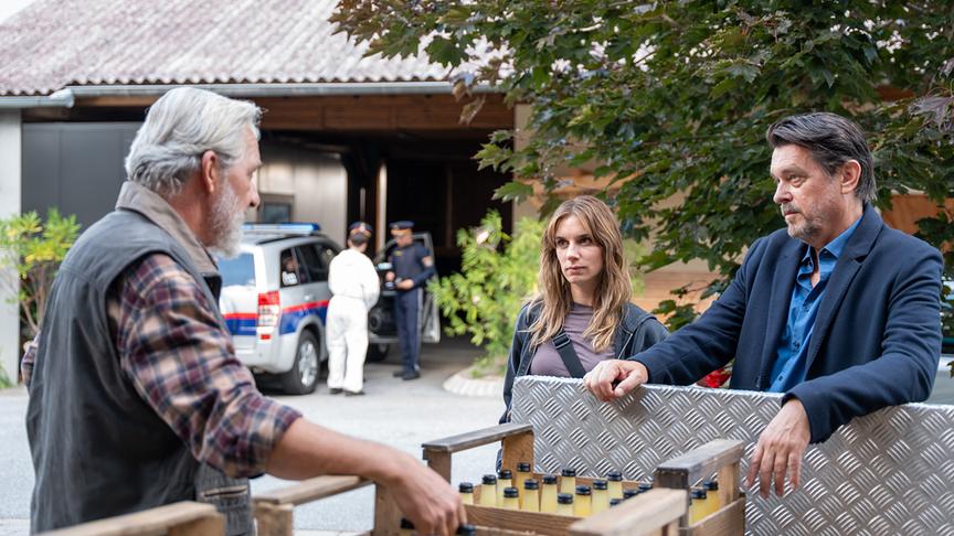 Hary Prinz und Maya Unger  sprechen mit dem älteren Harald Posch vor einem Haus, während im Hintergrund Polizei und Spurensicherung im Einsatz sind.
