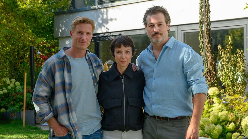 Golo Euler, Julia Koschitz und Julian Looman posieren im Garten vor einem modernen Haus im Rahmen der Dreharbeiten zu „Brennendes Schweigen“ (AT)
