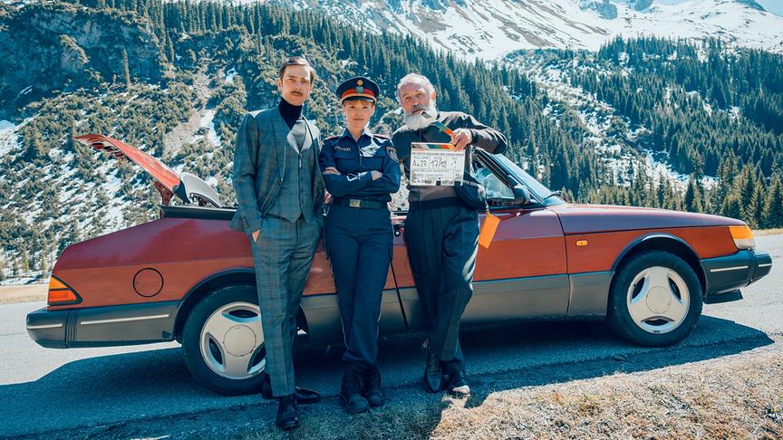 Stefan Pohl, Julia Koch und Karl Markovics posieren vor einem alten Auto in einer bergigen Landschaft am ORF-Landkrimi-Set zu „Die dritte Rochade des Jonas Horak“