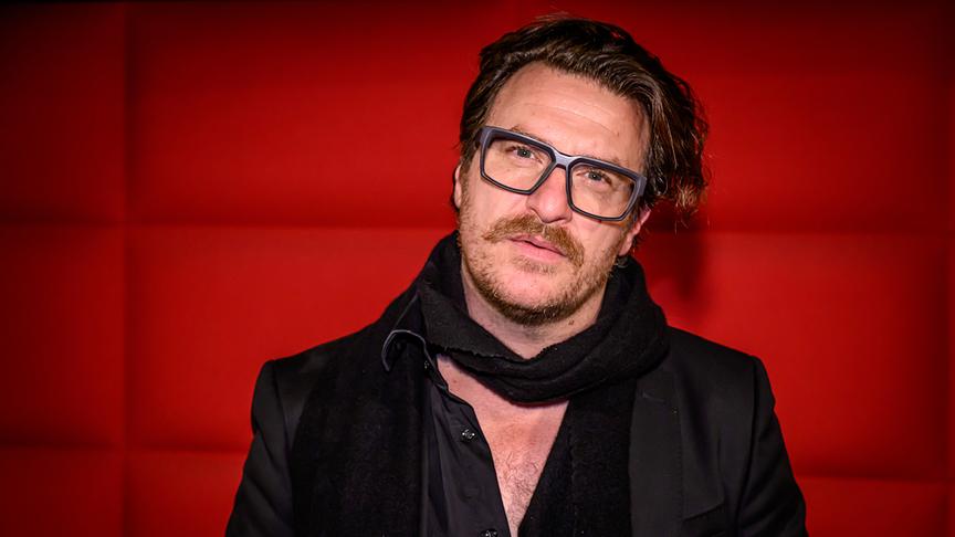 © ORF/Hans Leitner Parov Stelar aka Marcus Füreder bei der Kinopremiere für neues Filmporträt vor einer roten Stoffwand.