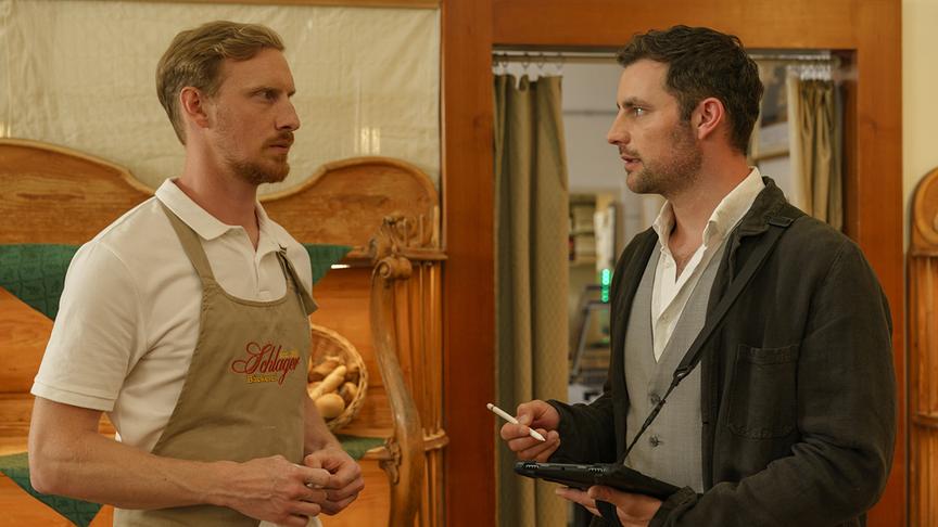Inspektor Felix Burger befragt Christian Schilling von der Bäckerei Schlager in einem rustikalen Ladenraum.