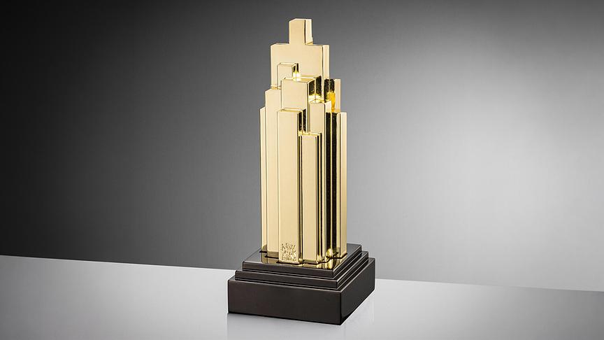 Die goldene Trophäe der „New York Festivals Radio Awards“ in Form eines Wolkenkratzers auf einem schwarzen Sockel vor neutralem Hintergrund.