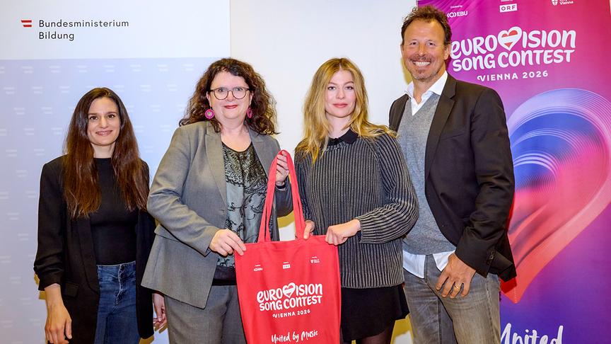 Dorothee Freiberger, Doris Wagner, Zoe Straub und ESC-Executive-Producer Michael Krön posieren vor Bannern des Bildungsministeriums und des Eurovision Song Contest 2026, wobei zwei von ihnen gemeinsam eine rote ESC‑Einkaufstasche halten.