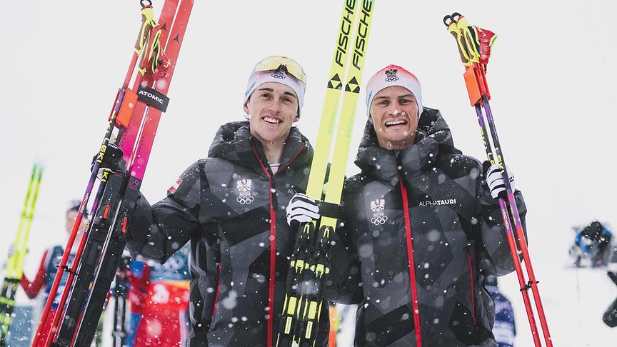 Bronzemedaillengewinner Stefan Rettenegger und Johannes Lamparter in österreichischen Teamjacken halten im Schneefall ihre Langlaufski und Stöcke hoch,  nach dem Langlauf Bewerb für den Nordische Kombination Team Sprint der Männer im Rahmen der Olympischen Winterspiele in Tesero.