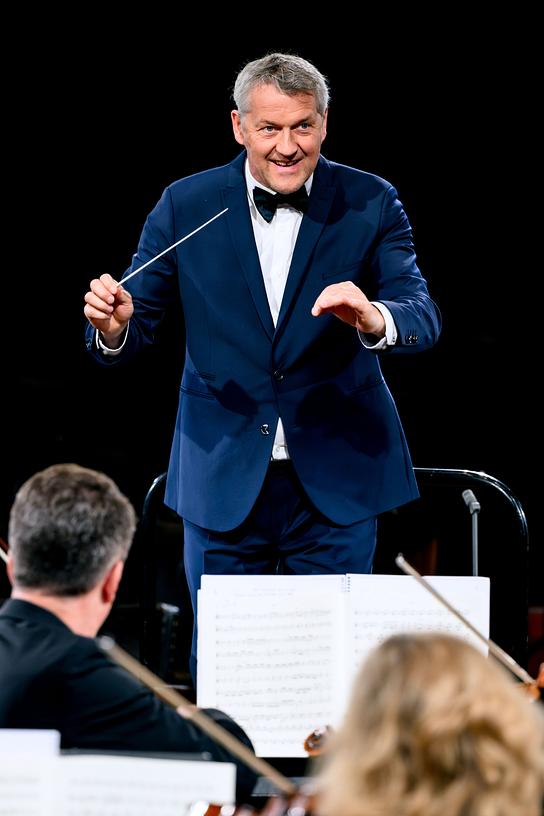 Chefdirigent Markus Poschner im blauen Anzug und mit Fliege leitet mit Taktstock das ORF Radio-Symphonieorchester Wien.