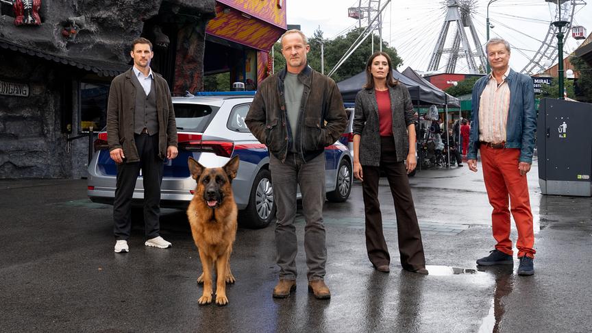 © ORF/MR Film/Petro Domenigg Ferdinand Seebacher, Maximilian Brückner, Doris Golpashin, Alfred Dorfer mit Hund Rex posieren im Wiener Prater vor einem Polizeiauto und dem Riesenrad im Hintergrund.