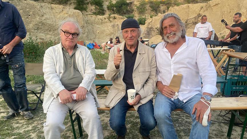 Michael Köhlmeier, Robert Dornhelm und Norbert Blecha sitzen auf Bierbänken vor einer Felswand
