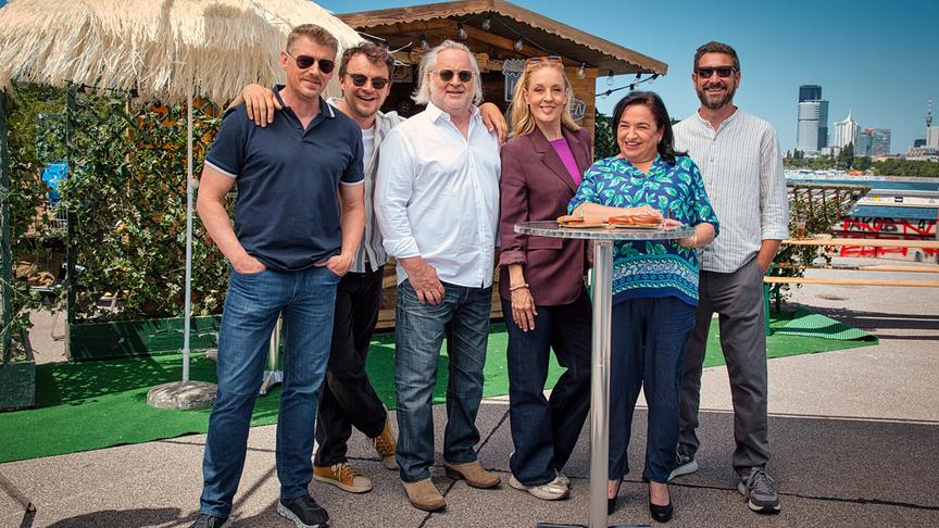 © ORF/ZDF/Satel Film/Thomas Kirschner Martin Gruber, Max Fischnaller, Gregor Seberg, Lilian Klebow, Maria Happel und Andreas Kiendl stehen an einem sonnigen Tag im Freien vor einer kleinen Hütte zusammen, mit einer Skyline von Wien im Hintergrund.