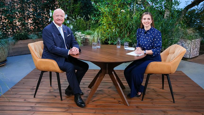 © ORF/Roman Zach-Kiesling Bundeskanzler Christian Stocker und Simone Stribl sitzen an einem runden Holztisch im begrünten Außenstudio der ORF-"Sommergespräche 2026".