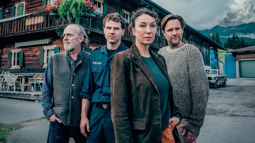 Sven-Eric Bechtolf, Noah L. Perktold, Ursula Strauss und Kai Ivo Baulitz stehen vor einem Bauernhaus in einer Alpenlandschaft zu "Tiroler Blut - Der erste Schuss".