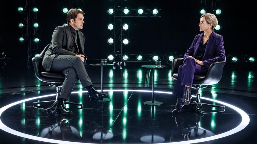 Ursina Lardi und Godehard Giese sitzen beim „Duell“ (AT) im Gespräch in Sesseln auf einer modern ausgeleuchteten Studiobühne.