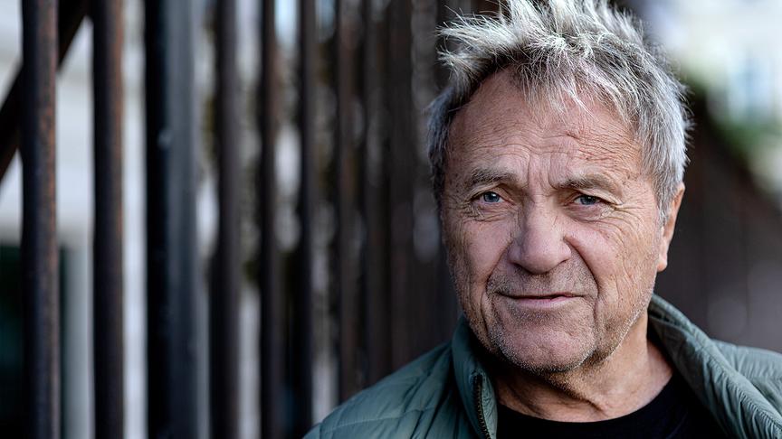 © ORF/Ulrik Hölzel Porträt von Wolfram Berger, aufgenommen draußen vor einem unscharfen Hintergrund mit dunklen senkrechten Streben.