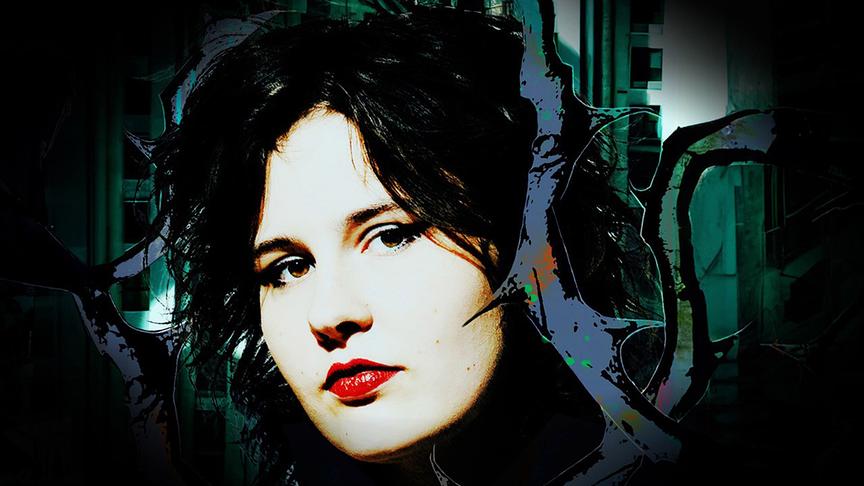 Porträt von Zelda Weber vor einem abstrakten, digital wirkenden Hintergrund mit dunklen Formen und grünlich-blauen Lichtakzenten.