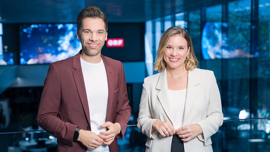 Philipp Maschl und Kathrin Pollak stehen lächelnd nebeneinander im ORF-Newsroom