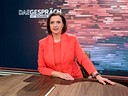 Susanne Schnabl sitzt in rotem Outfit an einem Holztisch im "DAS GESPRÄCH"-Studio