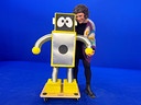 Esther und KIKI, eine selbstgebaute, gelb‑silberne Roboterfigur mit großen Augen, stehen in einem Studio mit blauem Hintergrund.