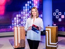Barbara Stöckl  steht im modernen "Stöckl live"-Studio zwischen zwei Pulten und hält eine Moderationskarte in den Händen, während im Hintergrund eine blau-rot-weiße digitale Grafik zu sehen ist.