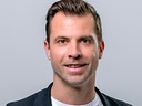 Andreas Ivanschitz steht lächelnd mit einem Mikrofon vor neutralem Hintergrund