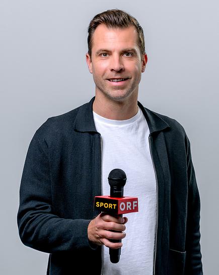 Andreas Ivanschitz steht lächelnd mit einem Mikrofon vor neutralem Hintergrund