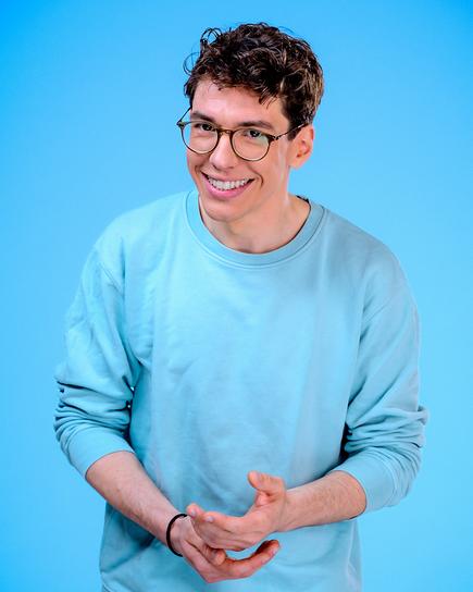 Christoph Hirschler in einem hellblauen Pullover steht vor blauem Hintergrund
