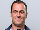 Michael Liendl steht vor grauem Hintergrund und hält ein ORF-Mikrofon in der Hand.
